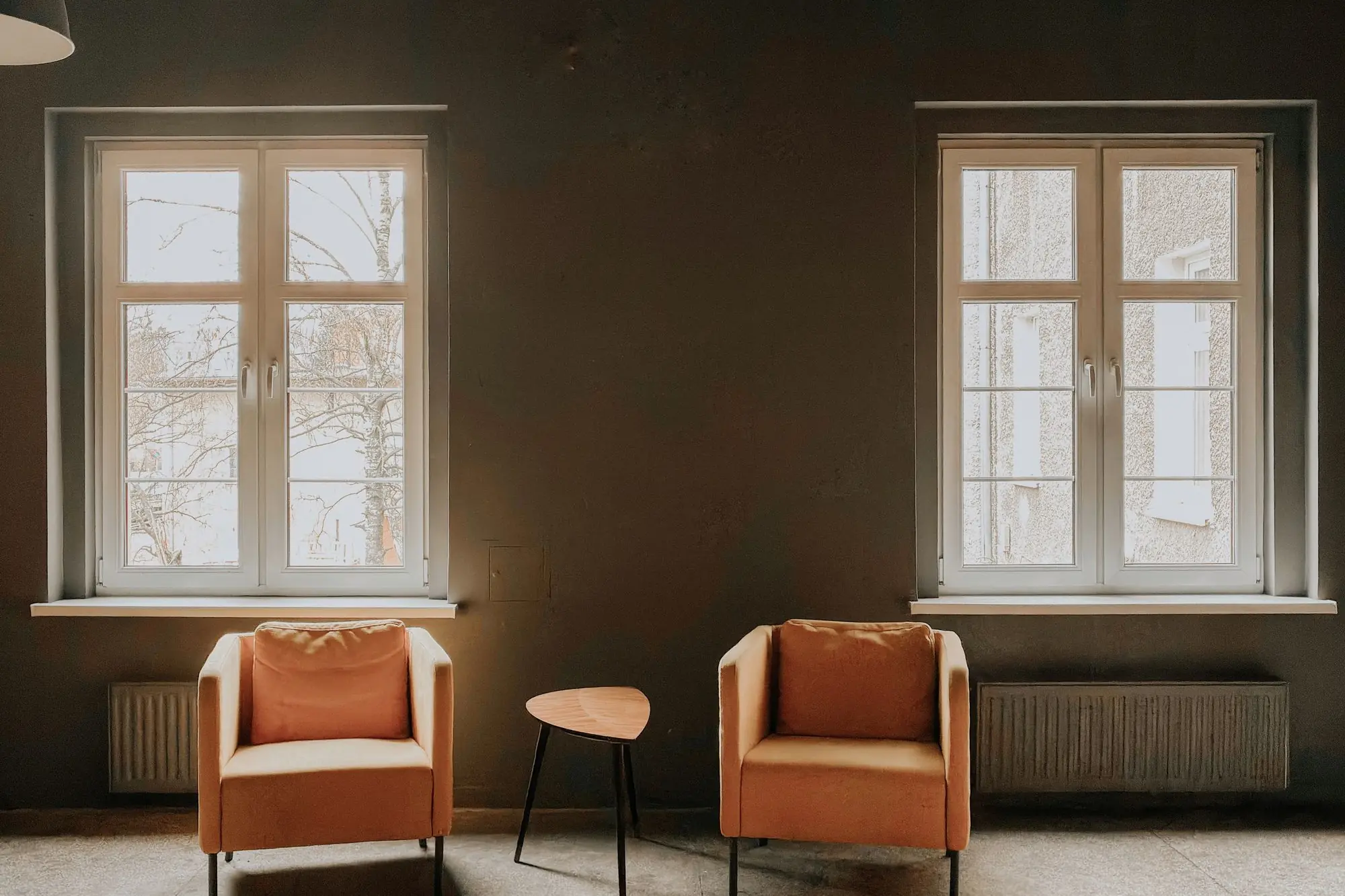 Dos butacas y una mesa baja junto a las ventanas de una sala tranquila